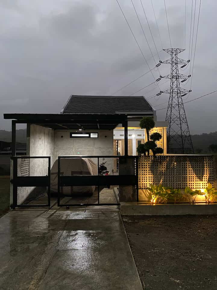 Gray and black 1K house exterior with metal gate and illuminated concrete roster wall, featuring terrace area under night lighting