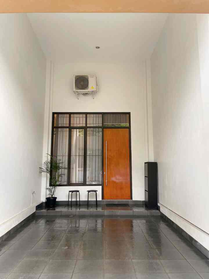 Modern entrance with white walls and black tiled floor, featuring a wood tone door, two black stools, and corner black storage cabinet