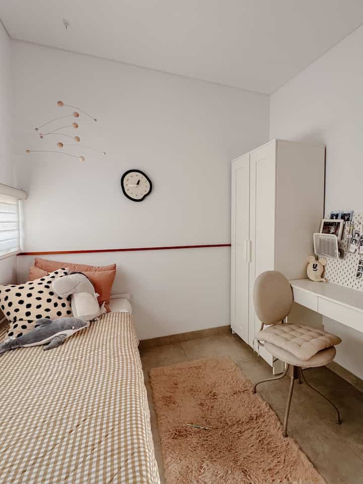 A simple and cozy bedroom for a single household in white and beige tones, featuring a bed, wardrobe, desk, and chair