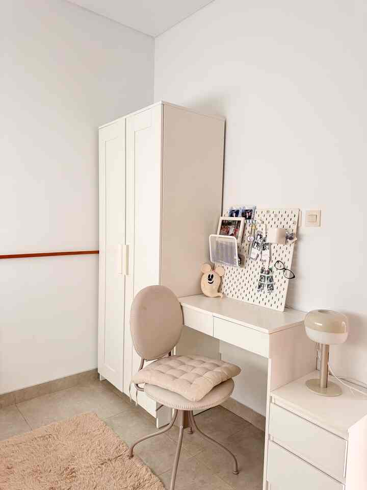 White and beige toned multi-use room featuring a white wardrobe, desk, and beige chair in a simple and clean setting