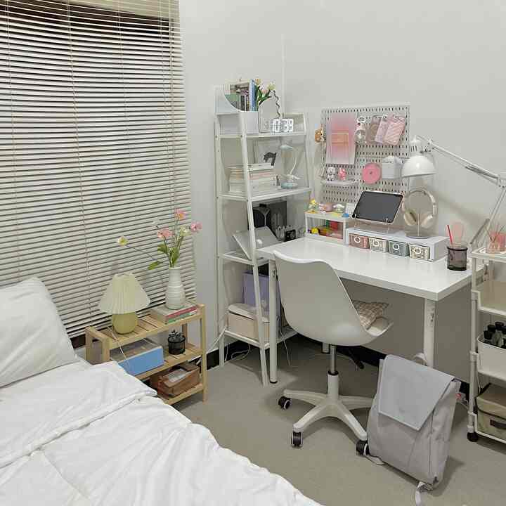 White and natural toned small bedroom featuring a desk, bookshelf, and chair arranged neatly for a quiet workspace
