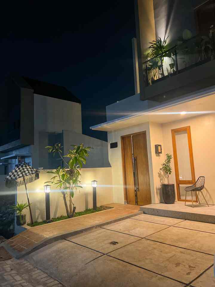 Modern entrance area with bright white walls and wooden door, featuring plants and lighting creating a cozy outdoor ambiance