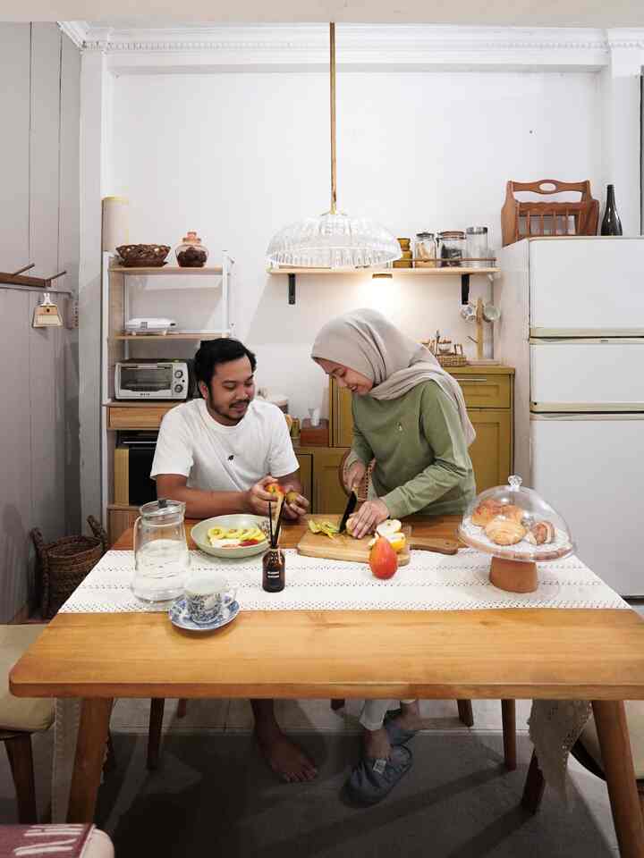White-walled dining room with natural wood-tone table, featuring two people sharing a cozy, warm atmosphere