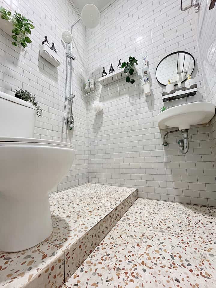 Modern bathroom dominated by white subway tiles and terrazzo floor, featuring round mirror and shower area enhancing the spacious feel in a small room