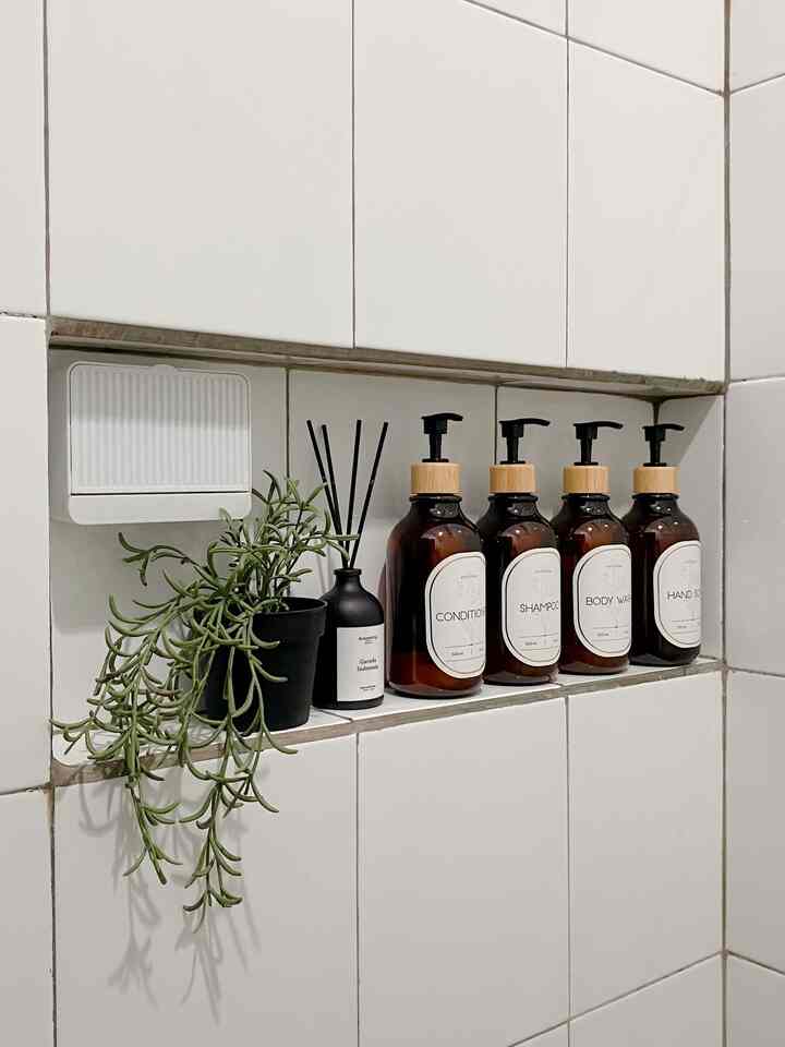 Bathroom niche with white tiled walls featuring a diffuser, potted plant, and amber pump bottles neatly arranged