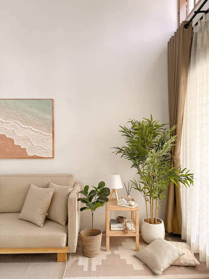 Ivory and beige toned living room featuring sofa, wooden side table, artificial bamboo plant, and natural cozy atmosphere