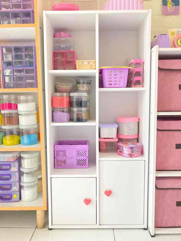 White and pink toned organized storage cabinet featuring various colorful craft supplies