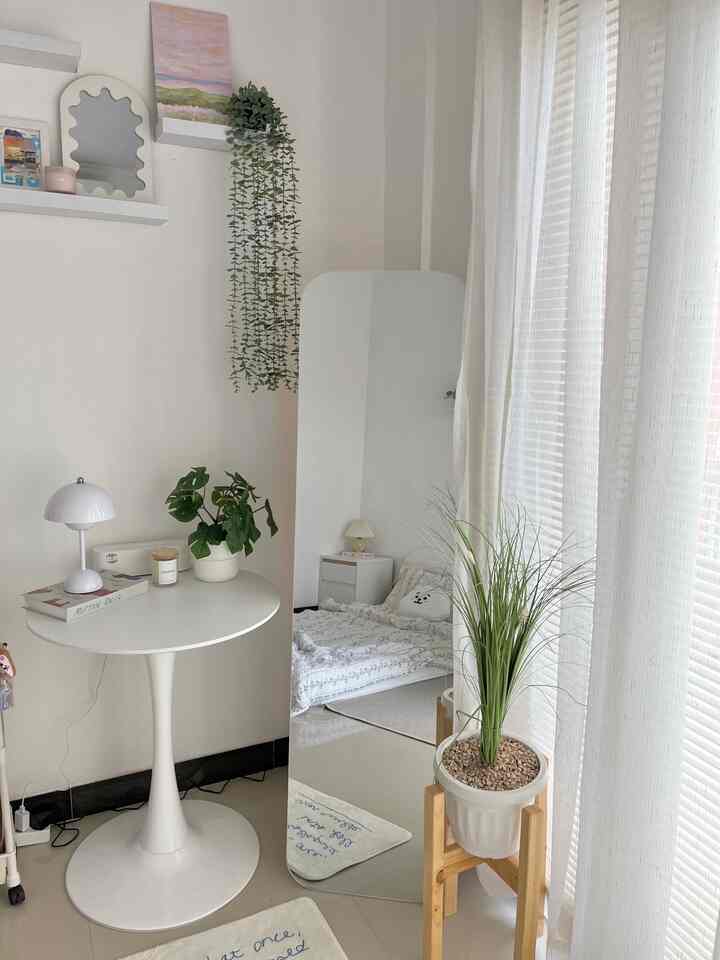 White-toned bedroom featuring a round table, standing mirror, and plants creating a natural modern space