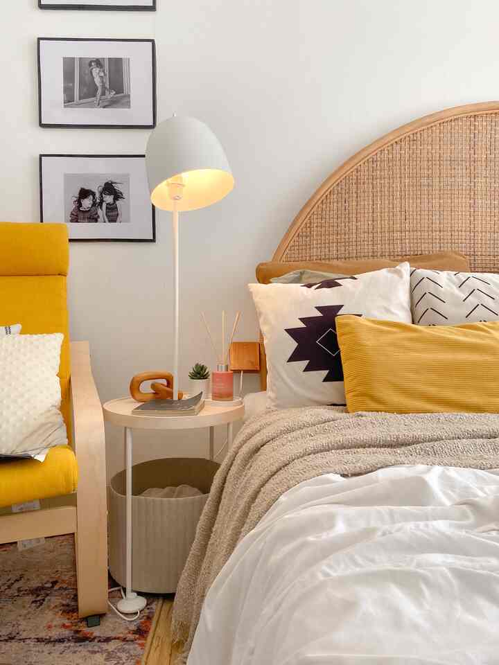 Natural tone bedroom featuring a rattan headboard, yellow armchair, and a white floor lamp, creating a cozy Nordic-style atmosphere