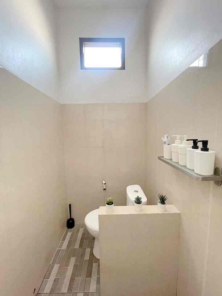 Small bathroom in white and beige tones featuring a toilet and neatly arranged shelf with toiletries, simple and clean space