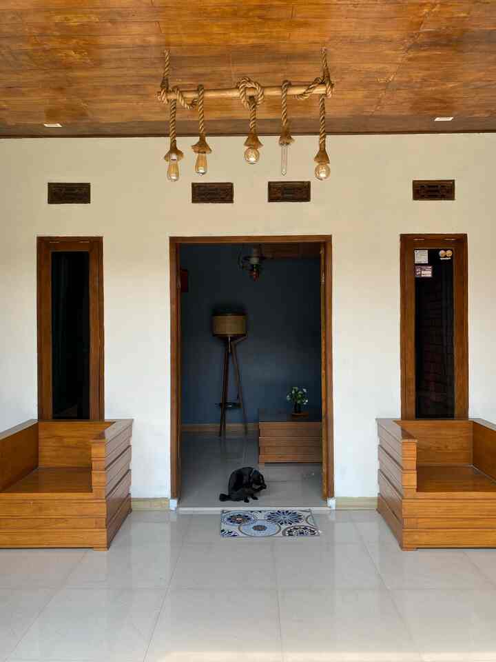 White walls and wood-tone furniture frame a living room entrance with a black cat sitting on the floor, creating a simple atmosphere
