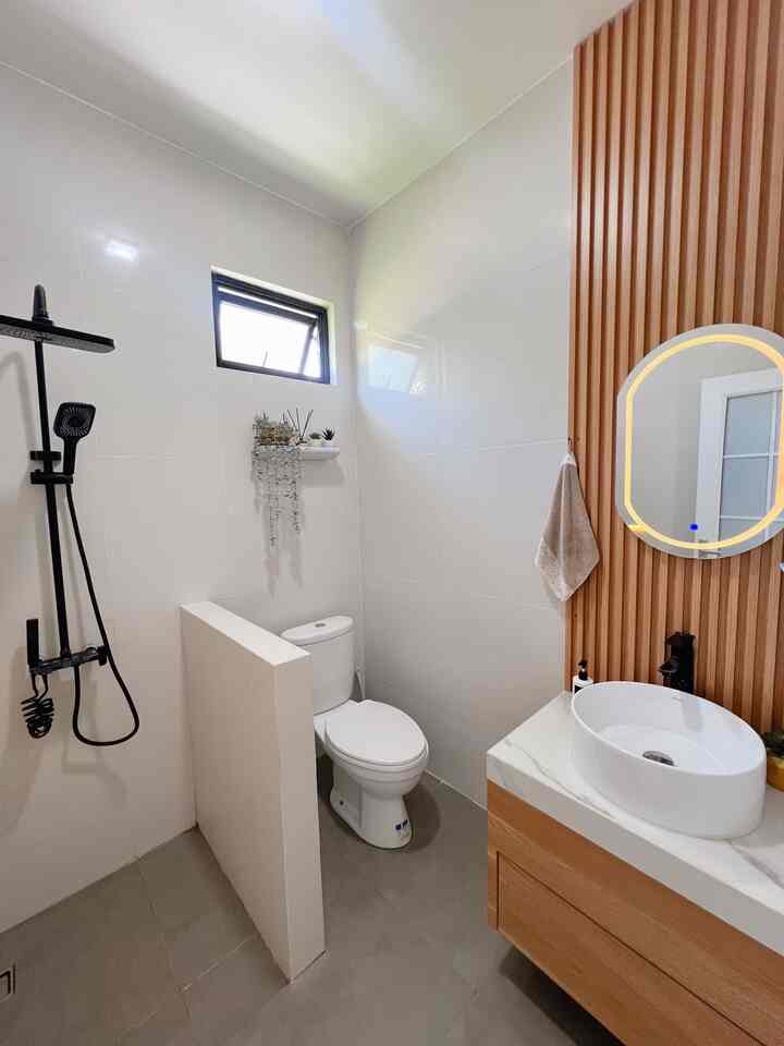 Compact bathroom featuring white walls, natural wood tones, with shower area, sink, and toilet efficiently arranged