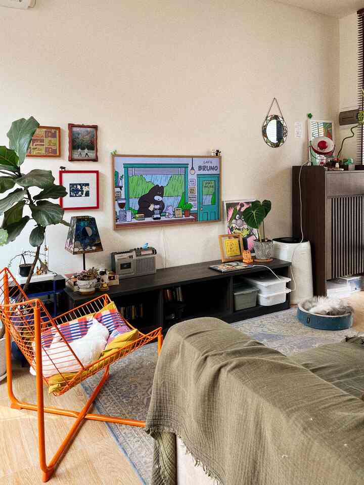 Natural color-toned living room featuring an orange chair, pet cat, plants, and framed artworks creating a cozy atmosphere
