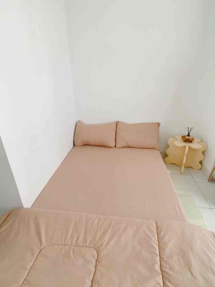 Beige toned bedroom featuring a neatly made bedspread and a uniquely designed side table in a clean space