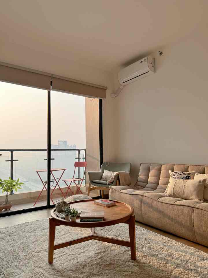 Beige-toned living room featuring a beige sofa, grey armchair, round wooden coffee table, and balcony with warm, inviting atmosphere