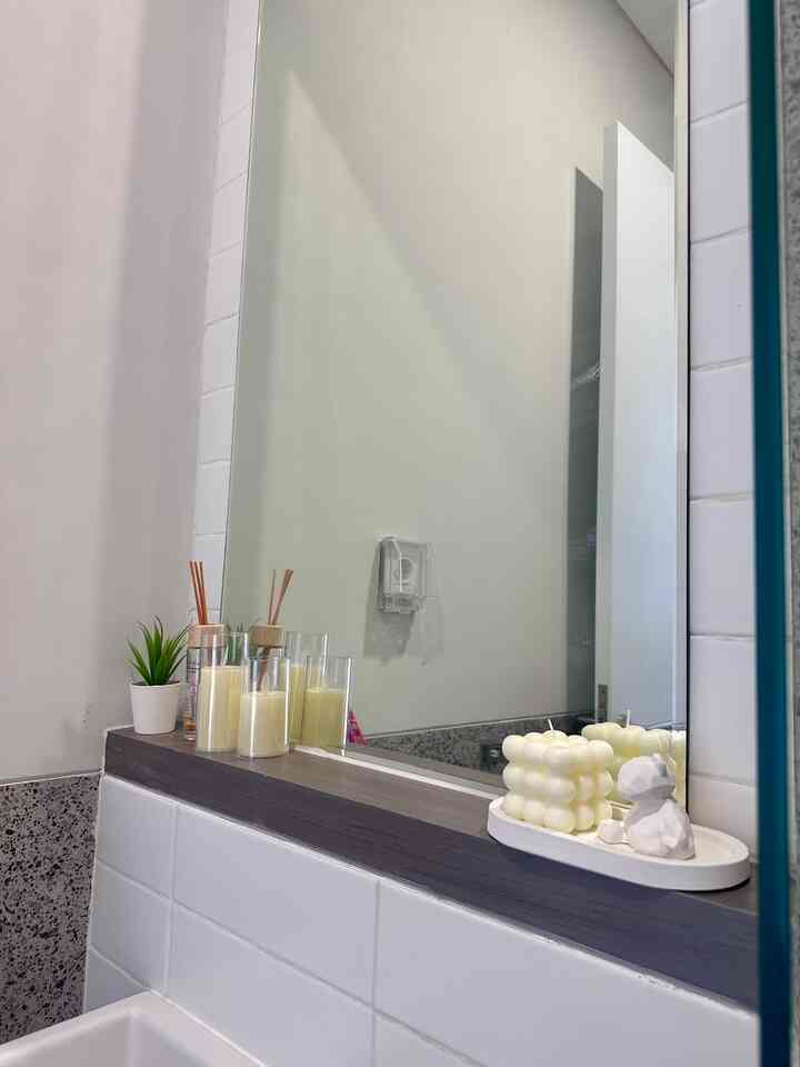 White and gray toned bathroom space featuring a large mirror shelf with candles, diffusers, and decorative objets creating a calm atmosphere