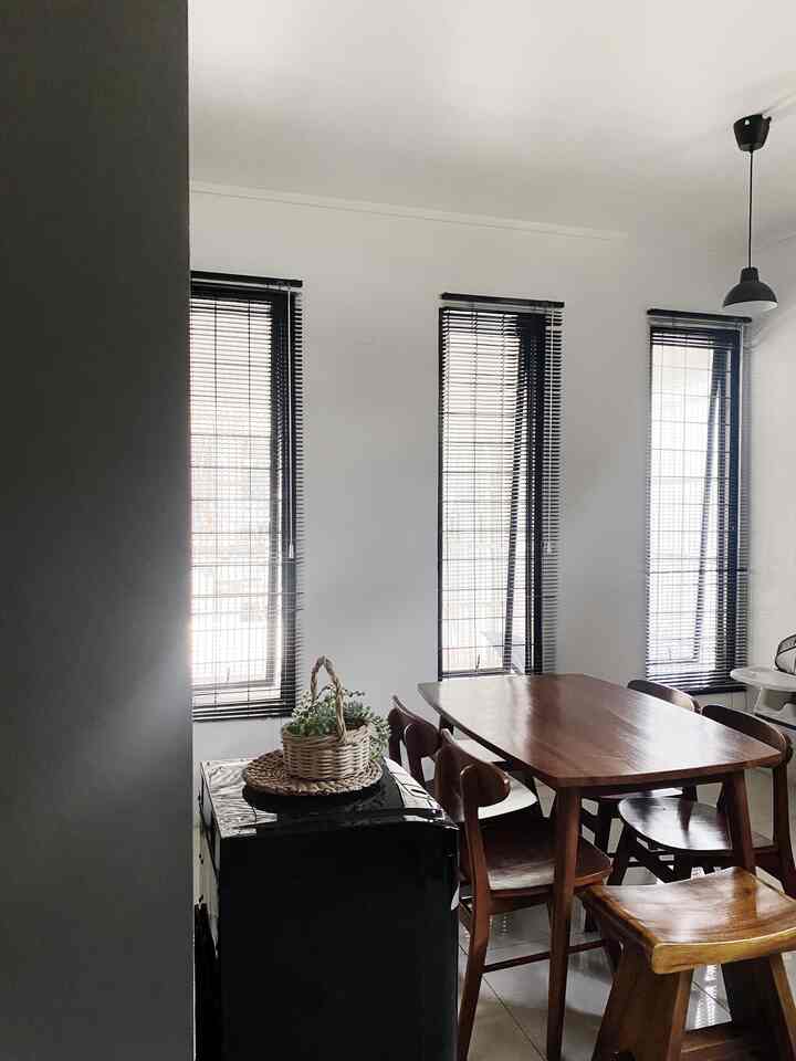 Natural wood tone dining room with white walls, featuring blinds on windows and a black cabinet, creating a clean atmosphere