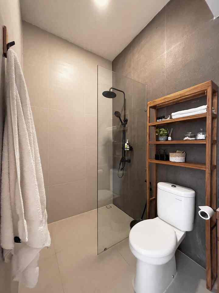 White and brown toned compact bathroom featuring wooden shelves and a transparent glass shower enclosure in a clean guest bathroom space