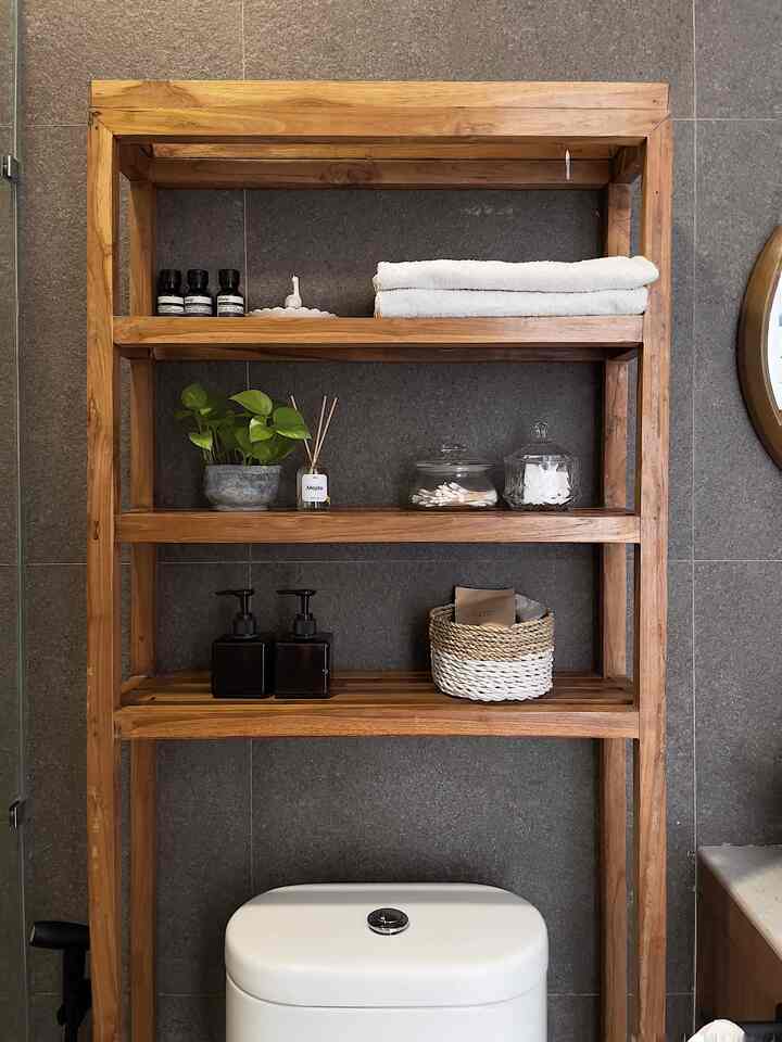 Bathroom with gray tiled walls and brown wooden shelving, featuring towels and diffusers arranged naturally