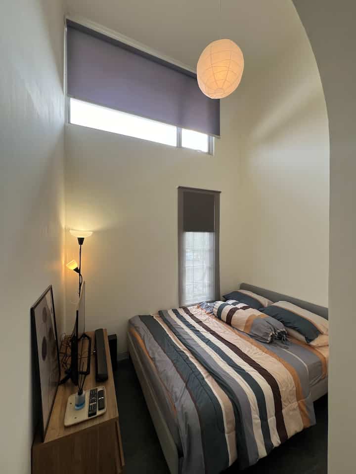 Natural-toned small bedroom featuring a large bed, modern lighting fixtures, and roller blinds with a simple aesthetic