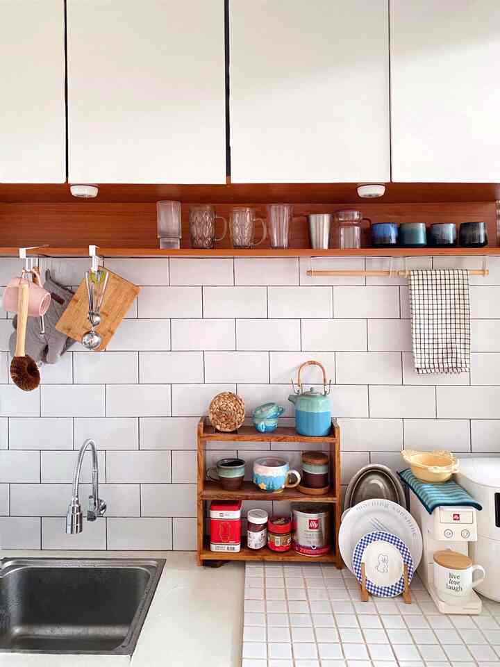 Bright kitchen space with clean white tiled wall and wood-tone cupboards, various mugs and teapot arranged creating cozy home cafe vibe