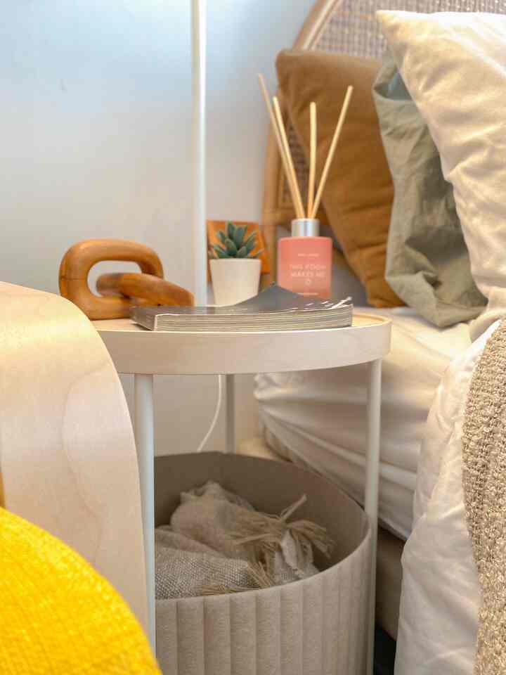 Natural color tone bedroom featuring a side table, pillows and blanket storage, with warm lighting accents