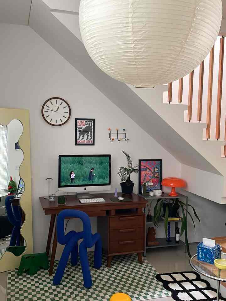 White-walled home office under stairs featuring a brown wooden desk and a unique blue office chair, creating a cozy and functional workspace