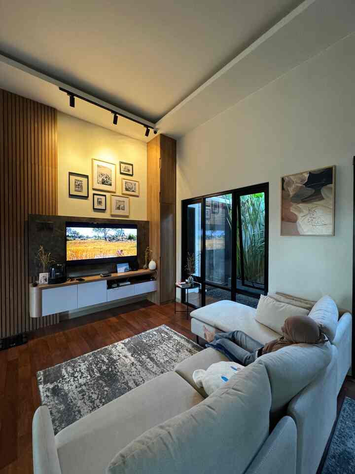 Cozy living room with warm wood tones and beige sofa, featuring TV and framed artworks for a stylish atmosphere