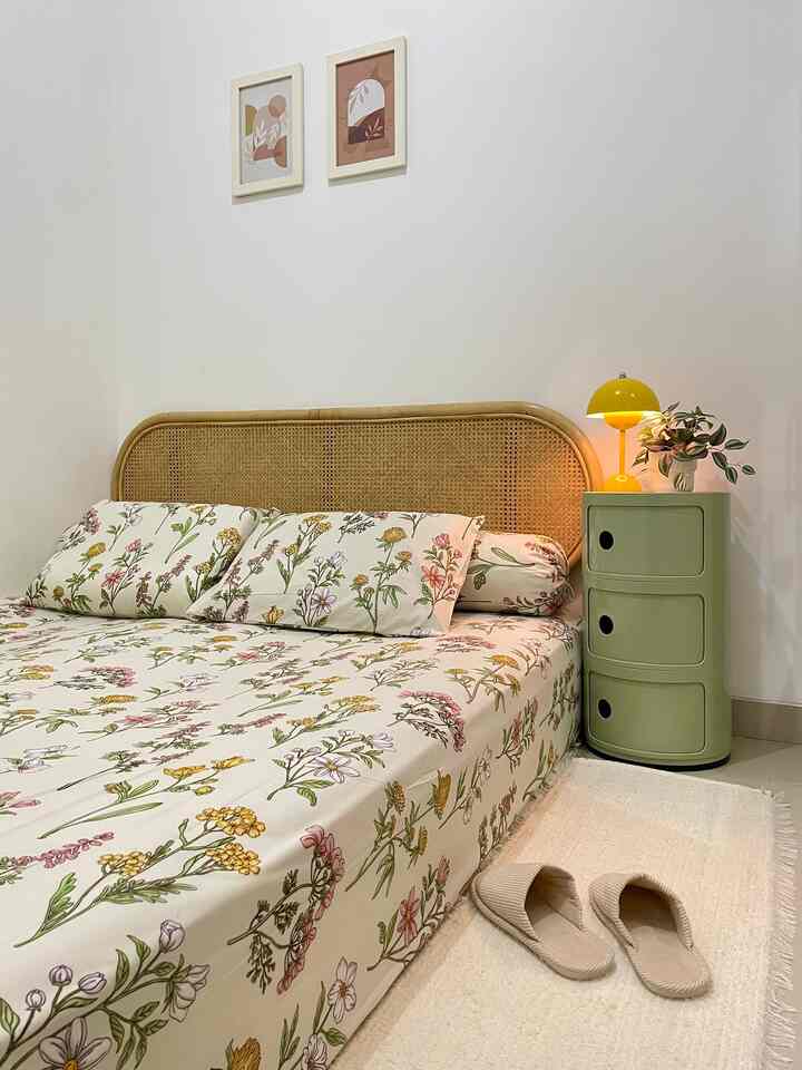 White walls and natural rattan headboard in a simple bedroom featuring floral bedding and yellow table lamp