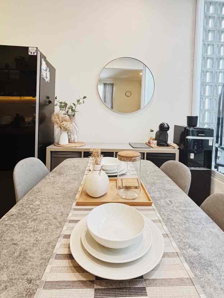 Bright white and brown toned dining room featuring a dining table with chairs, round wall mirror, and a home cafe setup, creating a clean modern space