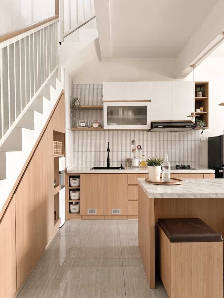 Natural tone kitchen space featuring wooden cabinetry and white tiled walls with a clean and cozy atmosphere