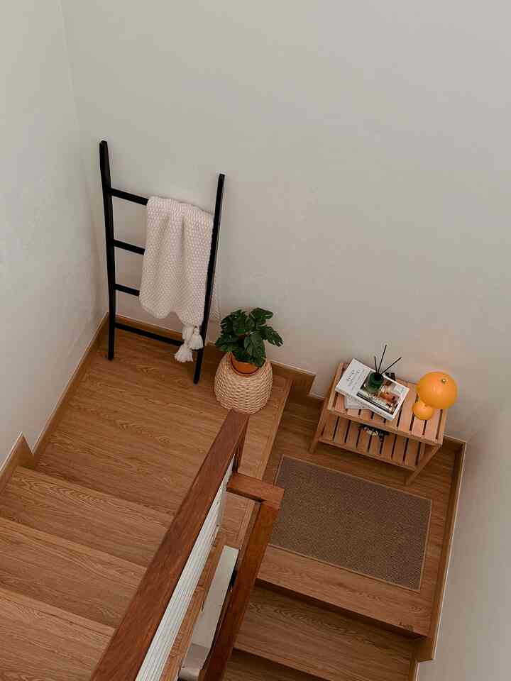 Natural wood-toned corner stair space with black ladder, green plant, and yellow table lamp creating a cozy atmosphere