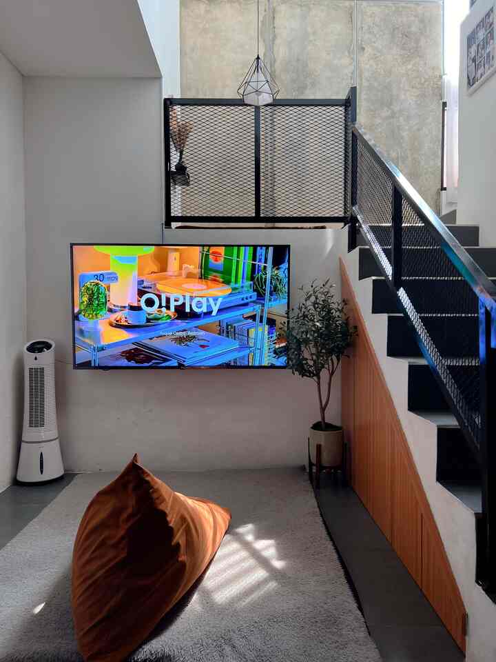 Black and brown toned living room featuring black metal stairs with ornamesh railing, brown bean bag, and wall-mounted TV in industrial style space