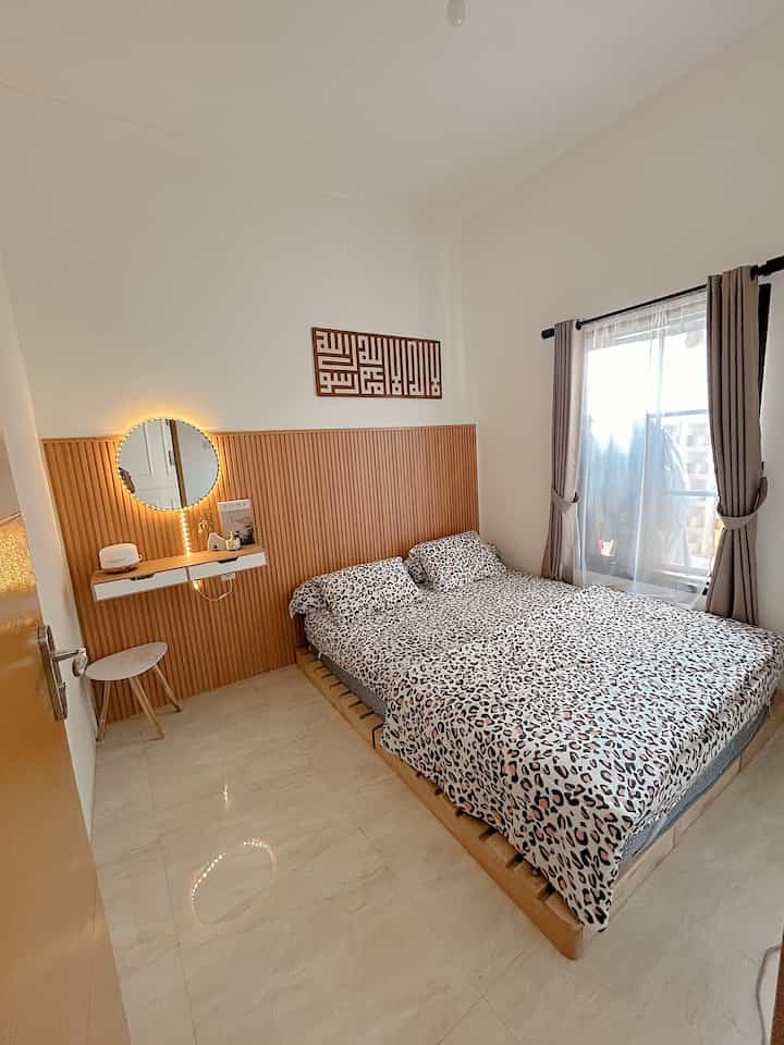 Bright white walls and wood-tone furniture create a cozy bedroom with beige flooring and curtained window for a calm atmosphere