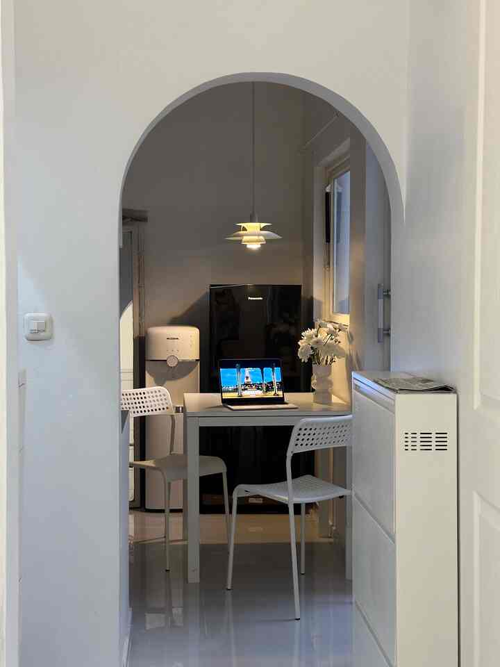 White-toned kitchen space featuring dining table, chairs, and laptop on table, creating a clean and modern home office atmosphere