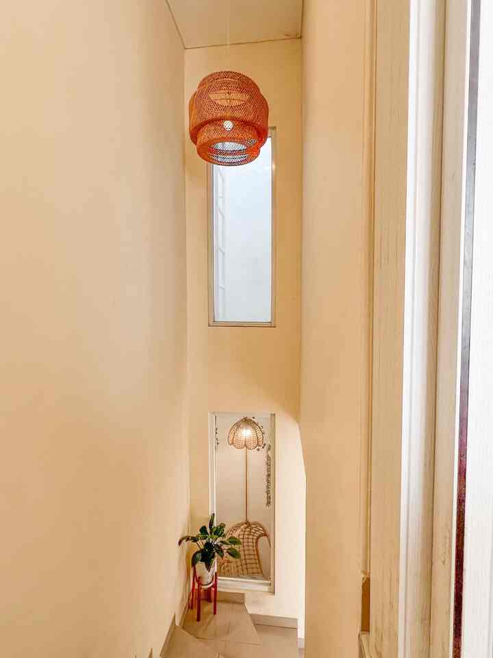 Beige-toned narrow and long hallway featuring rattan pendant light and plant stand with a natural atmosphere