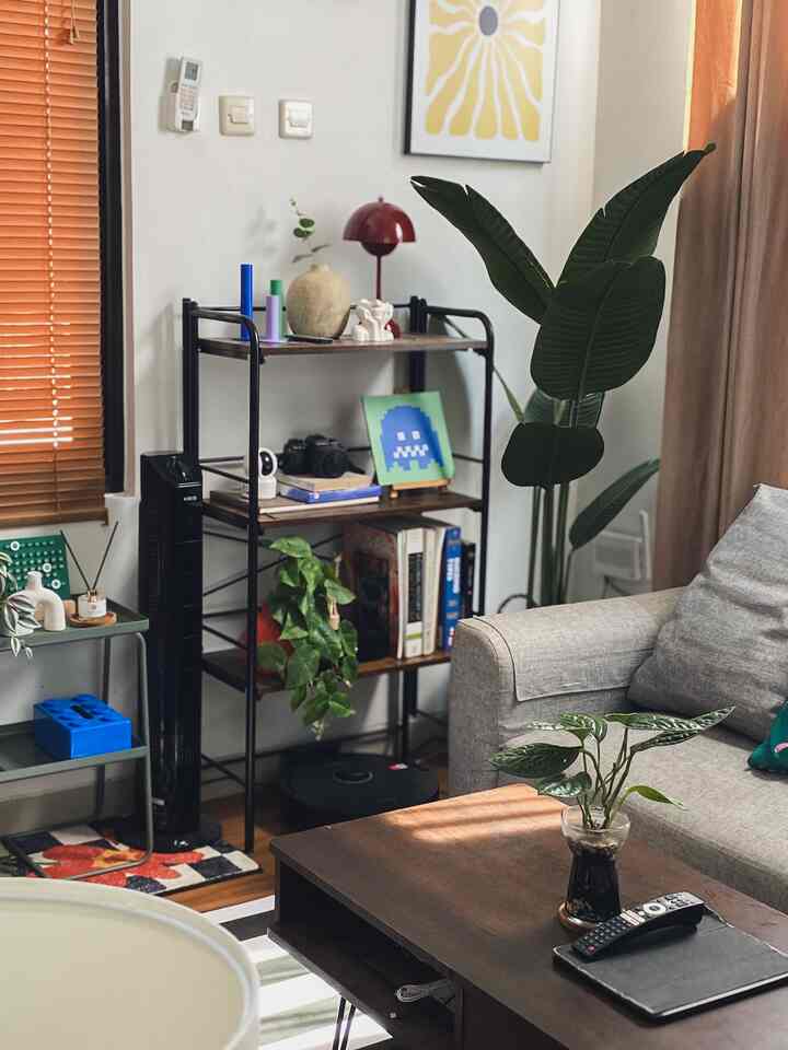 Natural tone living room with brown wood furniture, gray sofa, plants, and shelving unit