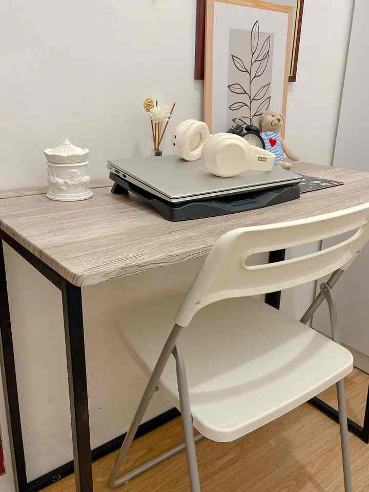 White and brown toned home office space featuring folding chair and desk with laptop, creating a simple workspace
