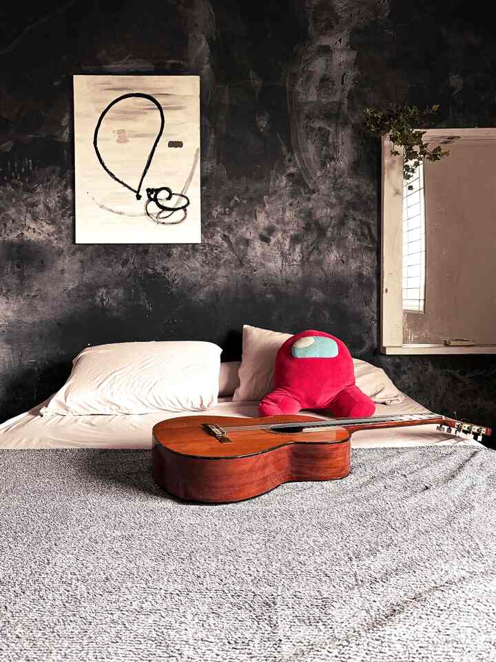 Vintage style bedroom with dark black textured wall, featuring a bed with an acoustic guitar and a red stuffed toy creating a cozy atmosphere