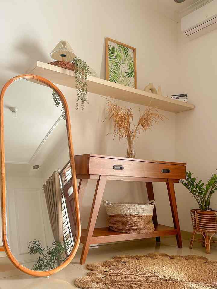 Beige-toned entrance space featuring wood tone furniture, a tall oval mirror, and plants creating a natural atmosphere