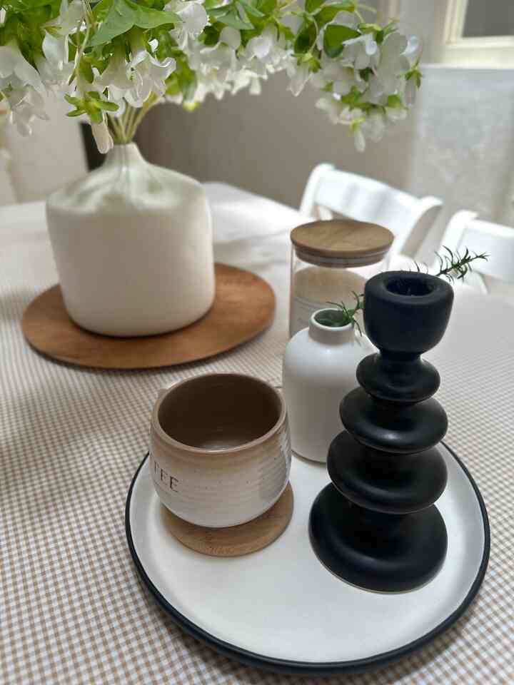 A simple and natural table decor space on a white and brown toned dining table featuring a vase, candle holder, and coffee cup