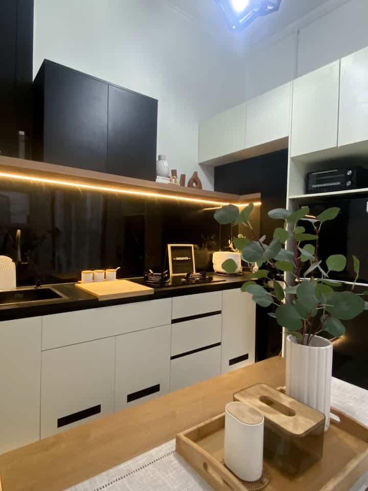 A modern kitchen featuring white and black cabinetry, natural wood tone table with plant decor under soft ambient lighting, minimal style