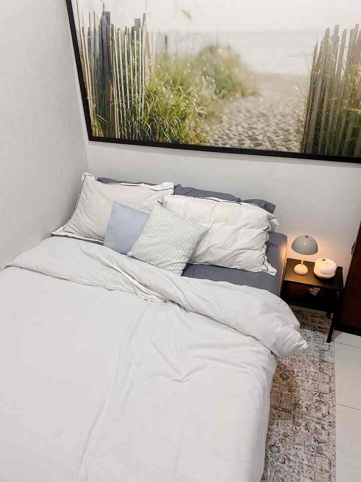 White-toned bedroom featuring a large central bed, nightstand on the right, and patterned rug creating a cozy atmosphere