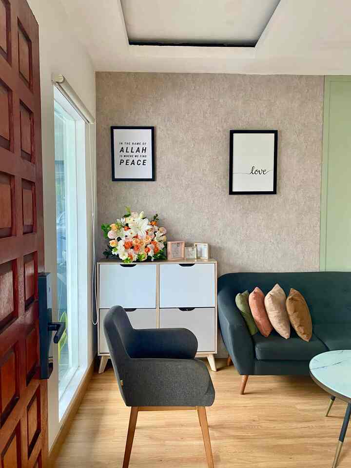 Cozy living room with beige textured walls, wood flooring, deep green sofa, and gray armchair with warm accents