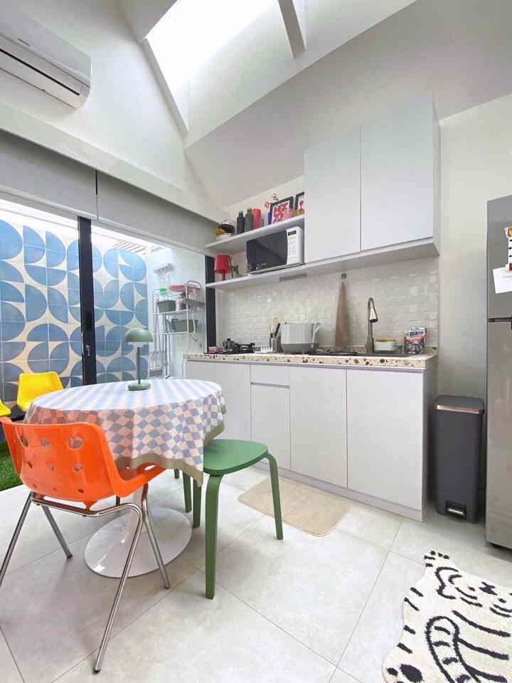 White-tone kitchen space featuring white cabinets, sink area, round dining table with colorful dining chairs in a clean design