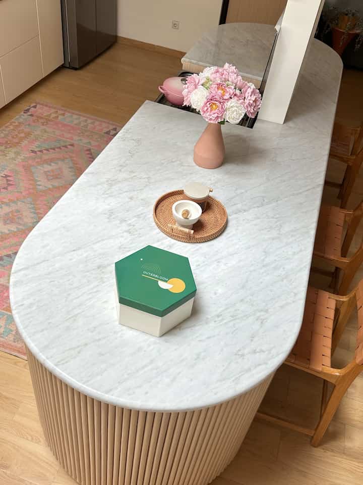 Natural wood tone flooring and Bohemian carpet, marble dining table with pink flowers create a cozy space