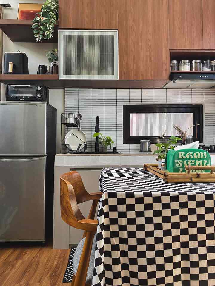 A cozy tiny kitchen with natural wood tones, featuring a dining table with a checkered tablecloth and a modern refrigerator