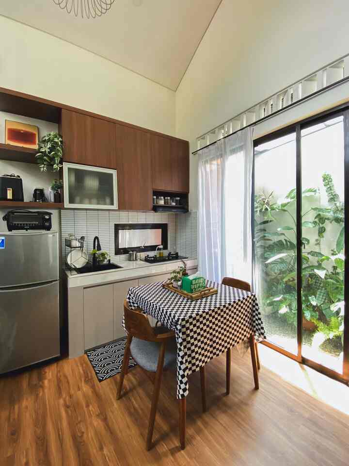 Bright white and warm brown kitchen featuring a dining table with chairs, large glass window with sheer curtains allowing natural light in, showcasing a natural atmosphere