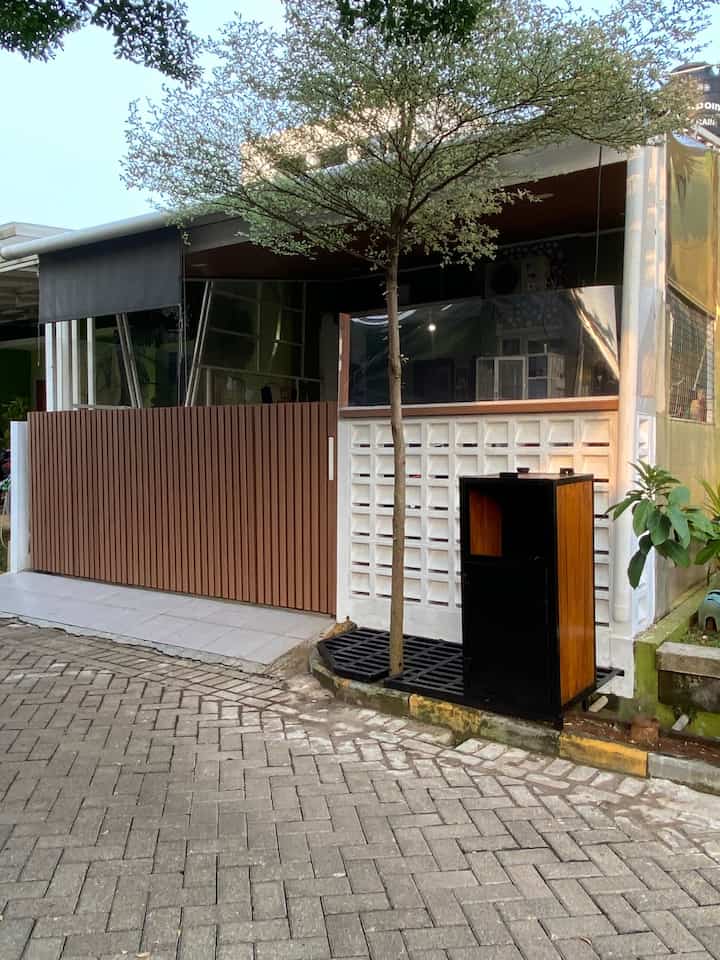 Exterior facade of a house featuring natural wood tone fence and white wall, with a tree and cozy outdoor atmosphere