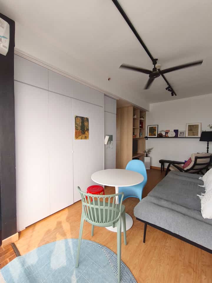 A compact kitchen and dining room in white and natural tones featuring a sofa bed and assorted chairs in a cozy space